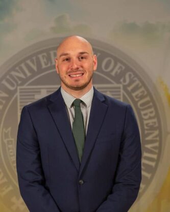 Aaron Foldi in a suit standing in front of a university seal.