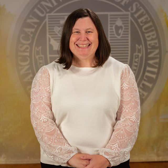 Anne Gabor wearing a white blouse standing in front of the university seal.