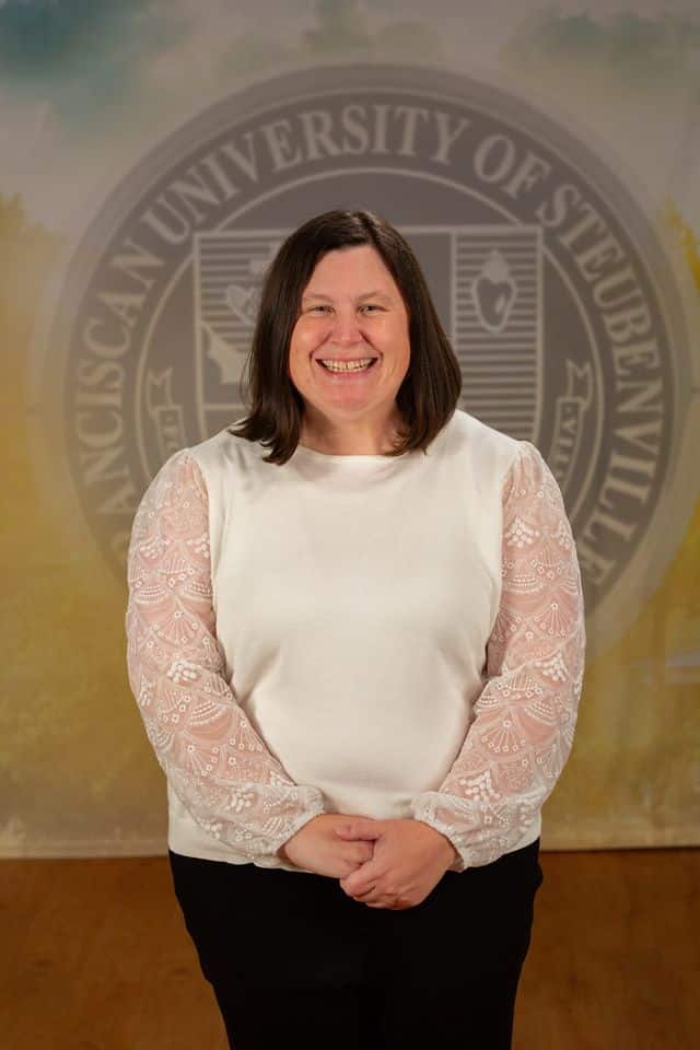 Anne Gabor wearing a white blouse standing in front of the university seal.