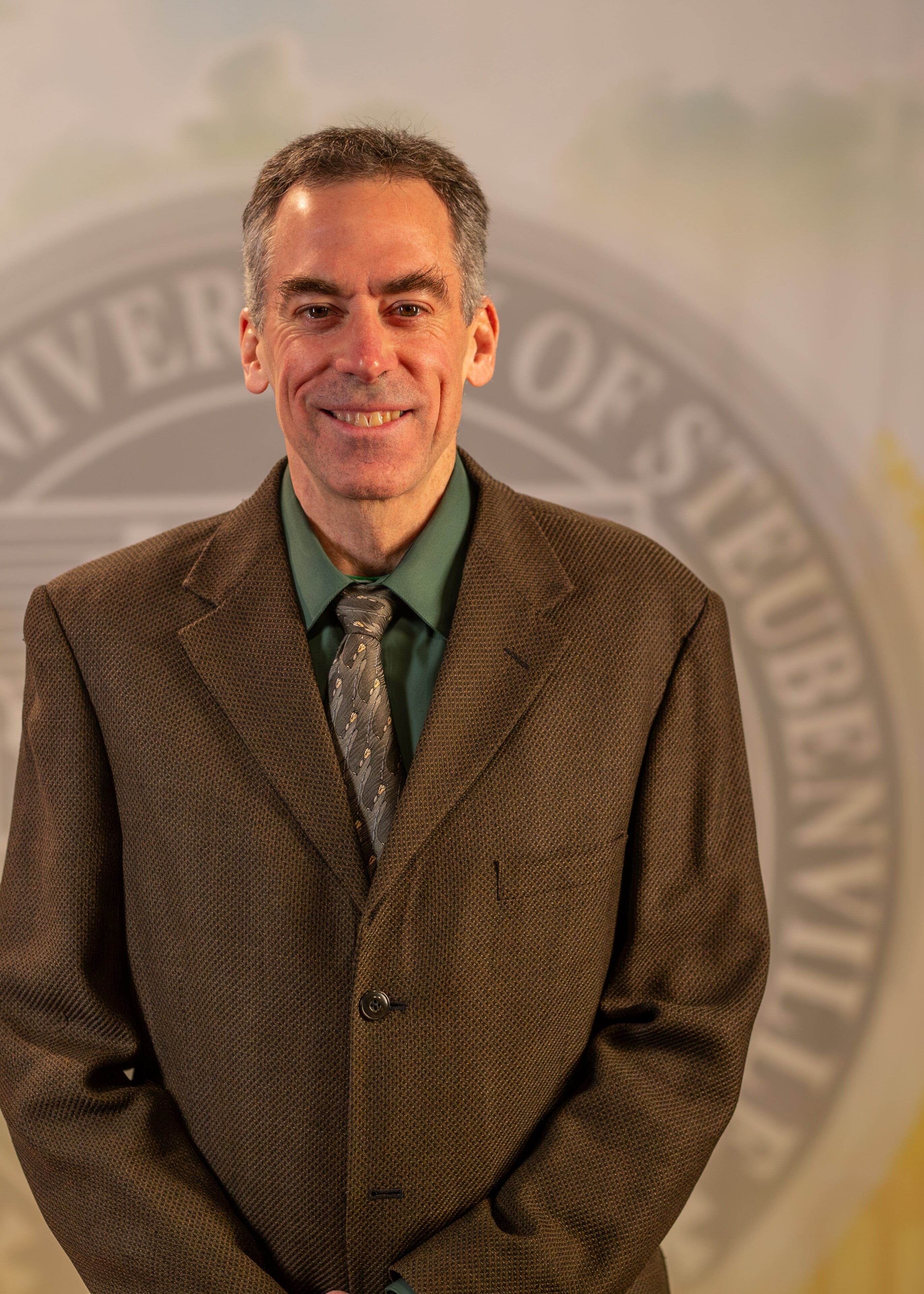 To Web – Dr. Ron Bolster FEB2025 –8 Dr. Ron Bolster standing in front of the Franciscan University of Steubenville seal.