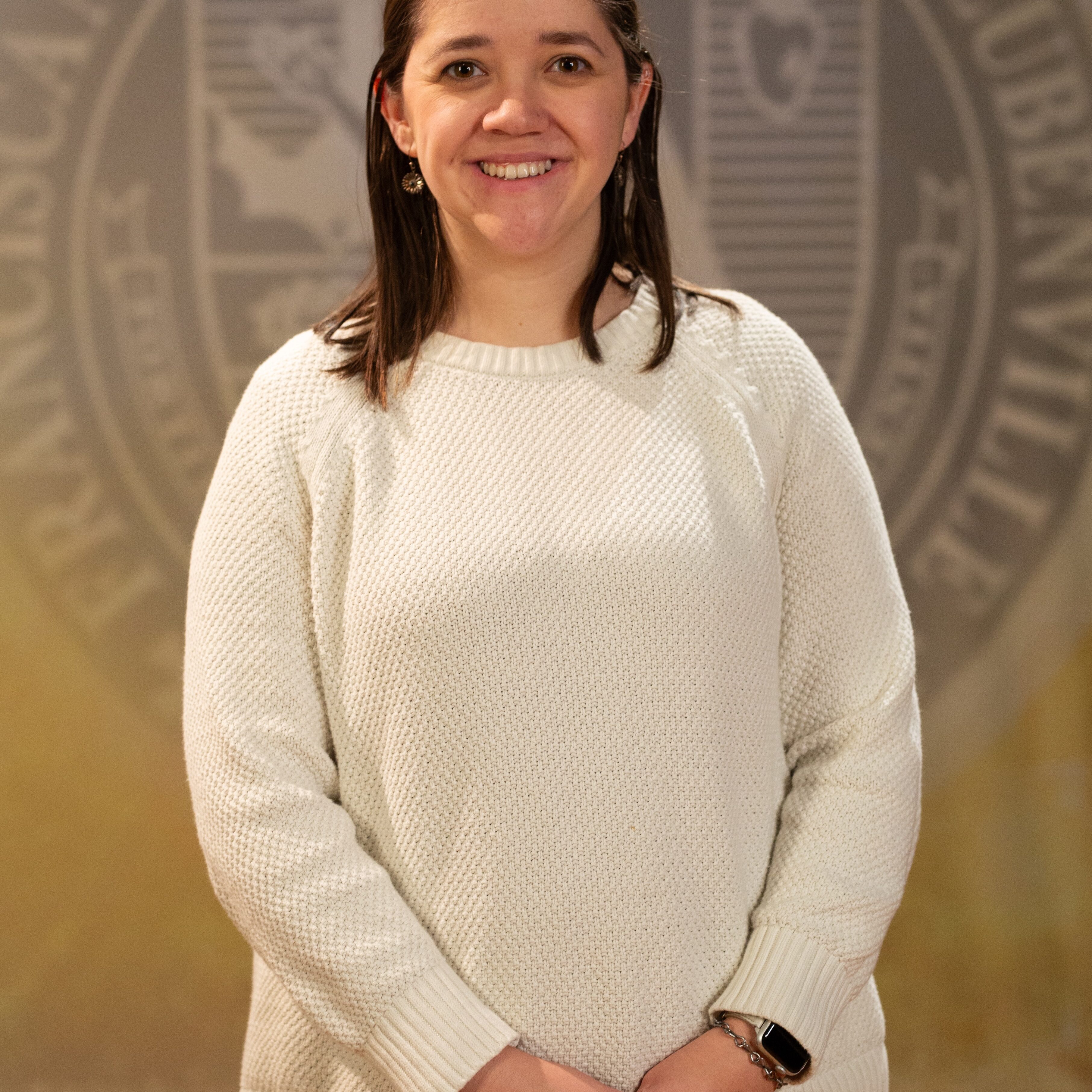 Faculty portrait of a Dr. Katherine Holler standing in front of the Franciscan University of Steubenville seal.